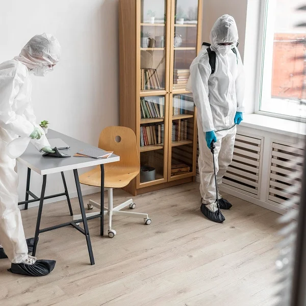 Deux personnes en vêtements de protection nettoient une pièce.