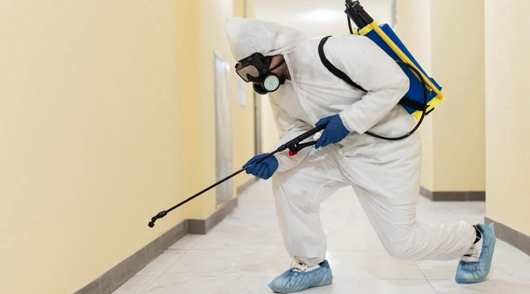 Un homme en combinaison blanche pulvérise un produit dans une pièce.