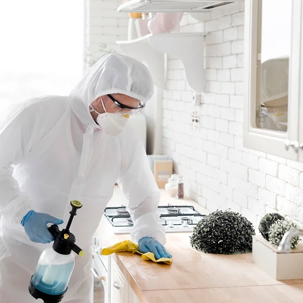 A man in a white protective suit cleans a counter with disinfectant, ensuring a safe and sanitary environment.