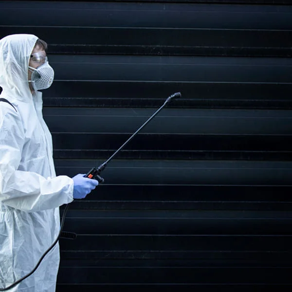 A man in a white protective suit and mask sprays a wall with a chemical solution.