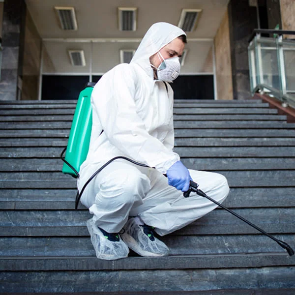 Un homme en costume blanc et équipement de protection pulvérise avec un pulvérisateur vert.