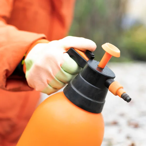 Une personne en veste orange tient un pulvérisateur orange.
