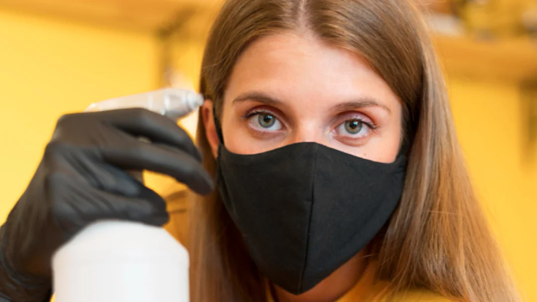 A woman in a black face mask holds a spray bottle, ready to clean or disinfect her surroundings.