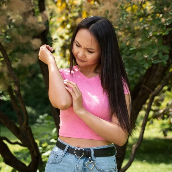 Femme en chemise rose et jeans se tenant debout dans un parc verdoyant.