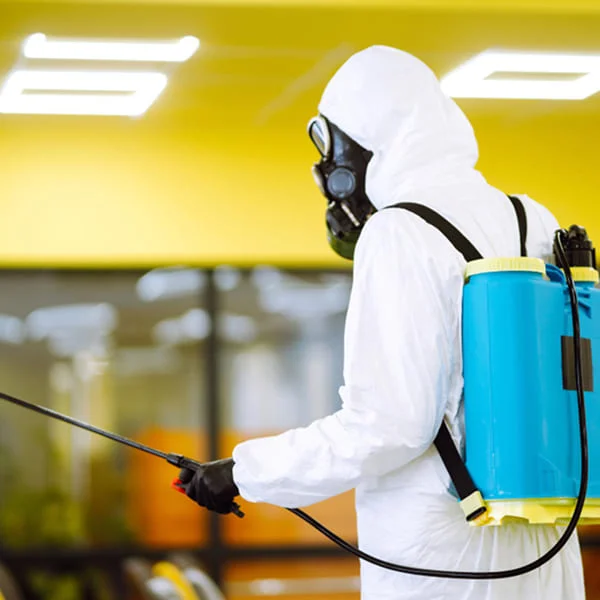 A man in a white protective suit sprays disinfectant in a room, ensuring a clean and safe environment.