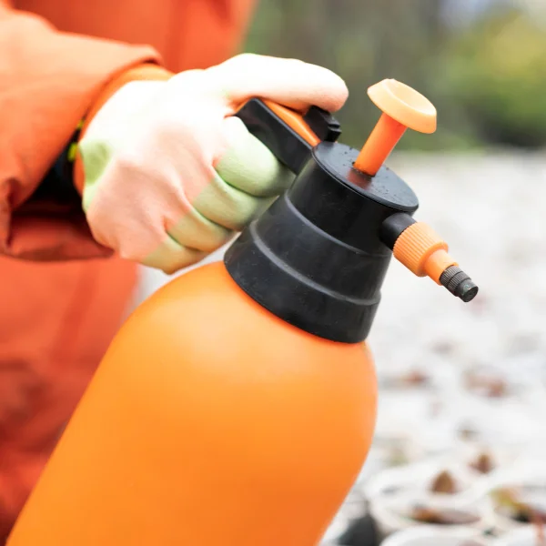 A person in an orange jacket holds an orange spray bottle, standing against a neutral background.