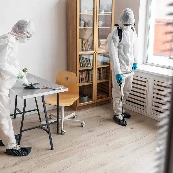 Two individuals in protective gear cleaning a room as part of an extermination service in Montréal.